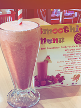 A tall pink smoothie beside the Tasty Cafe smoothie menu